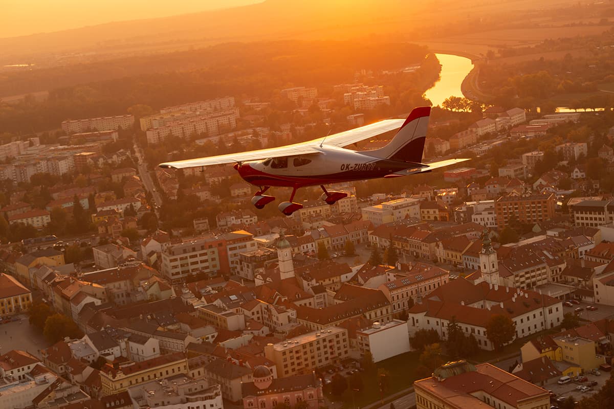 Bristell B8 above a town and river at sunset