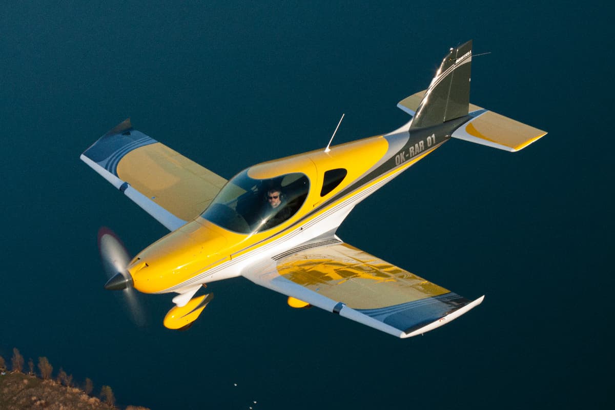 Yellow Bristell Classic banking in flight over a lake