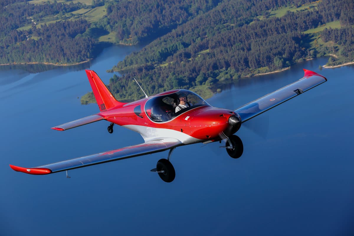 Bristell TDO cruising over a lake and wooded shoreline